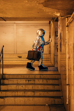 Spaceman in the city at night walking in underpass with suitcase and takeaway coffee