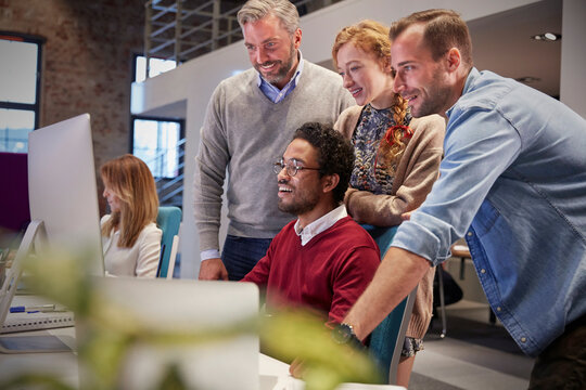 Colleagues looking over shoulder of young man working in modern office