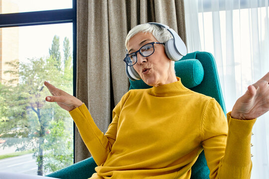 Senior woman sitting in armchair, listening music with headphones