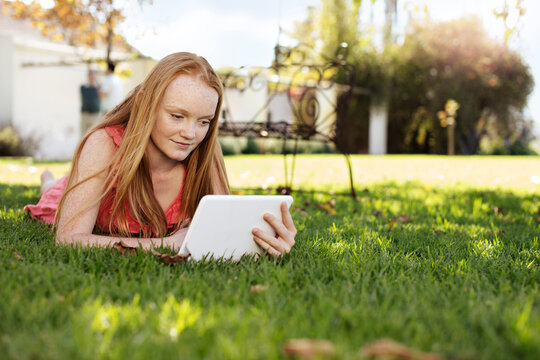 Grl with long red hair lying in grass with tablet