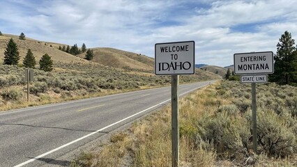 Rural highway with welcome to Idaho and entering Montana signs, open sagebrush hills and big sky, travel route marker for road trip planning, calm western mood
