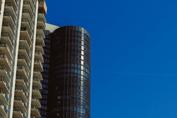 Modern buildings stand under a clear blue sky with a small airplane flying in the distance on a sunny day in an urban area