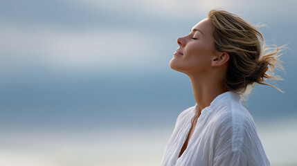 Obraz premium Peaceful woman with eyes closed breathing fresh air outdoors as symbol of mindfulness, relaxation, wellness, and mental health balance.