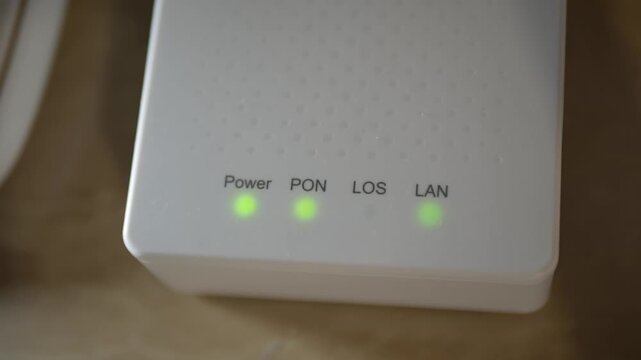 Close-up of GPON fiber optic converter with green LED indicators blinking. Optical network terminal working in real time. High-speed internet connection, FTTH broadband and telecom technology concept.