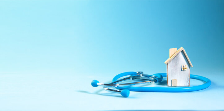 Miniature house and stethoscope on blue background with copy space