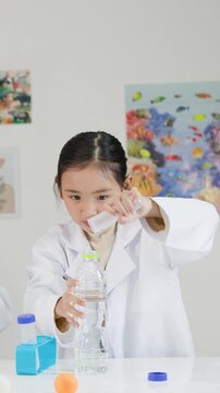 Asian Schoolgirl Performing Bernoulli's Principle Science Experiment with Water Bottle