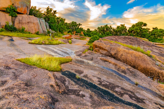 A winding dirt path leads through the scrub brush and mesquite trees at the base of the granite formations in the Texas Hill Country.