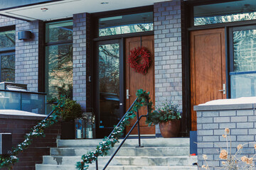 Decorative entrance in winter with dark bricks, wooden doors, wreath, and green garland near a snowy outdoor setting