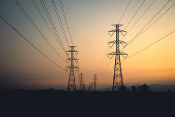 Silhouette of high-voltage electric transmission towers and power lines against a beautiful sunset sky with orange and purple hues.