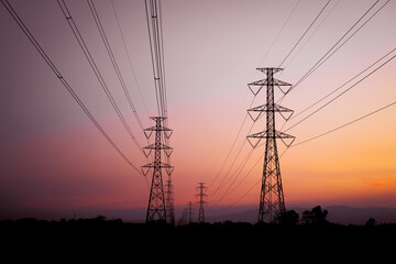 Silhouette of high-voltage electric transmission towers and power lines against a beautiful sunset sky with orange and purple hues.