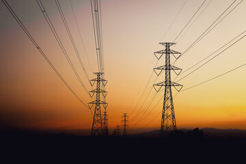 Silhouette of high-voltage electric transmission towers and power lines against a beautiful sunset sky with orange and purple hues. © elsa 
