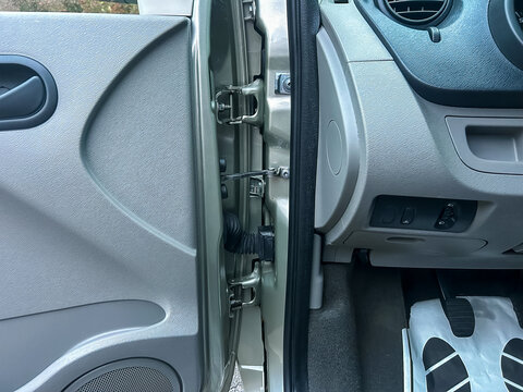 Car door interior shows latch mechanism with detailed view of the door handle, panel, and flooring during daylight, showcasing the workings of a vehicle entry system