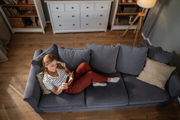 Woman relaxing on sofa reading book at home