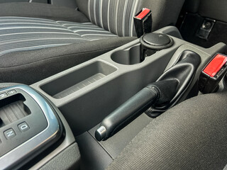 Obraz premium Car interior features center console with gear shift, cup holder, and seatbelt fasteners in a vehicle parked indoors during the day