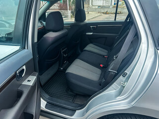 Interior view of a silver vehicle showing the backseat area with clean seats and floor mat in a parking setting during daylight