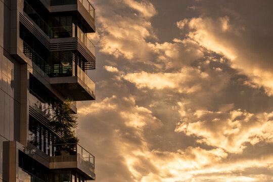 Apartment building with balcony facade in urban city at sunset beneath dramatic clouds and wide sky giving minimal copy space for residential architecture use