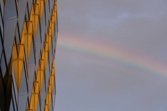 Abstract urban facade with reflective pattern and subtle rainbow under clouds and open sky presenting modern architecture with minimal copy space background