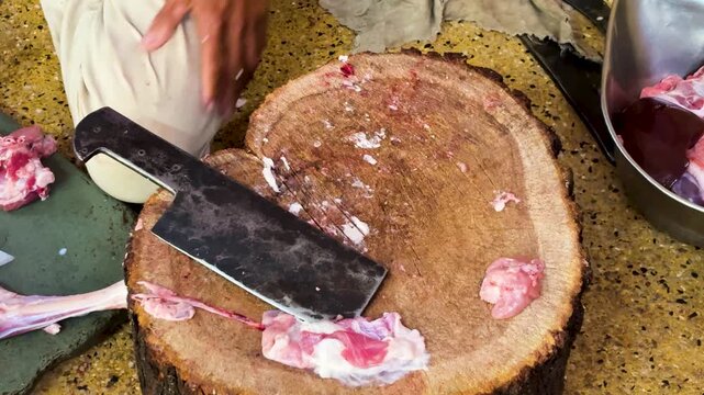 butcher chopping raw meat on wooden block with heavy cleaver at market