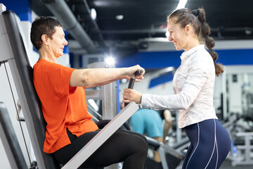 Personal trainer guiding senior woman on chest press machine