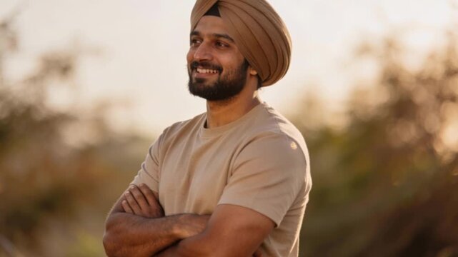 Smiling indian man wearing turban arm crossed confident beard standing sunset outdoor field park sunlight golden hour profile male sikh punjabi happy