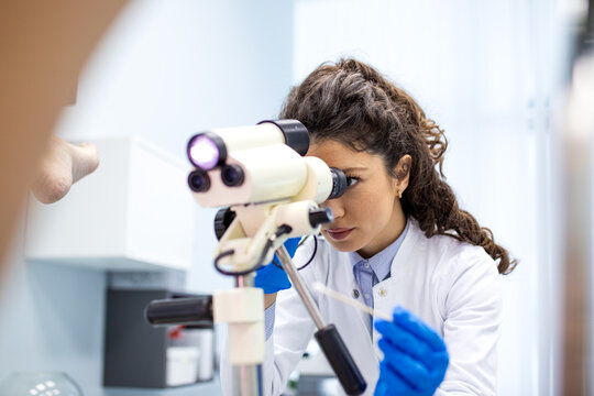Gynecologist performing colposcopy exam. Female doctor looking through colposcope for cervical screening in medical clinic. Diagnostic procedure, healthcare and reproductive medicine concept.