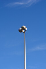 A tall white metal pole with two round street lamps stands under a clear blue sky with a faint white cloud