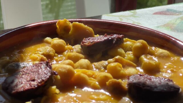 Steaming hot tripe and chickpea stew with blood sausage in a traditional clay bowl, a classic Spanish comfort food recipe