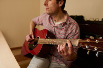 Obraz premium Man Adjusting and Changing Guitar Strings on Red Acoustic Guitar — Maintenance and Repair Practice