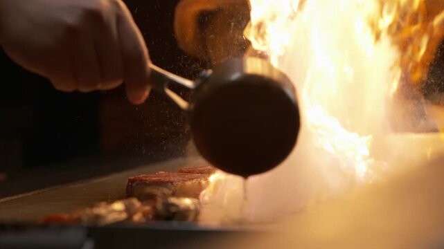 Chef searing meat on griddle with dramatic flame flare-up at a teppanyaki restaurant