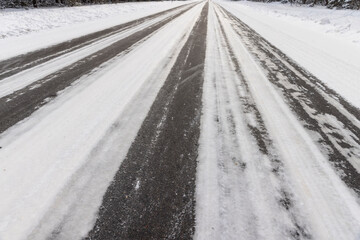 details of an asphalt road with car ruts and part of the road completely covered with ice and snow, part of the road for cars after snowfalls