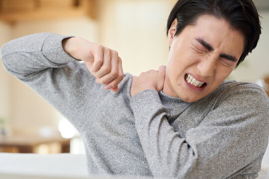 肩が痛くて腕を回すアジア人男性
