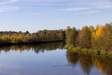 Obraz premium autumn river at sunset, beautiful deciduous trees on the riverbank before the fall of leaves, evening time before sunset