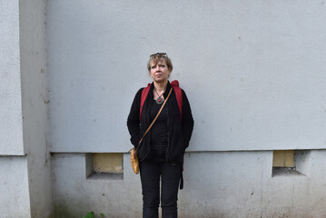 Middle-aged woman with blonde hair standing against a textured grey building wall © salajean