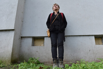 Middle-aged woman with blonde hair standing against a textured grey building wall © salajean