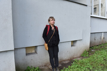Middle-aged woman with blonde hair standing against a textured grey building wall © salajean