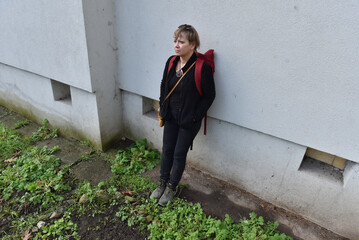 Middle-aged woman with blonde hair standing against a textured grey building wall © salajean