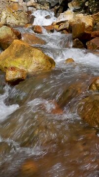 Vertical view Seamless Loop close-up of geothermal stream flowing over sulfur-stained volcanic rocks in Curug Cikawah geothermal area, Bogor, West Java, Indonesia.