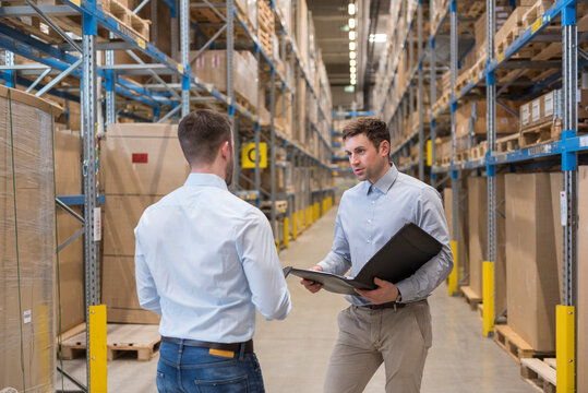 Two men with folder talking in factory warehouse