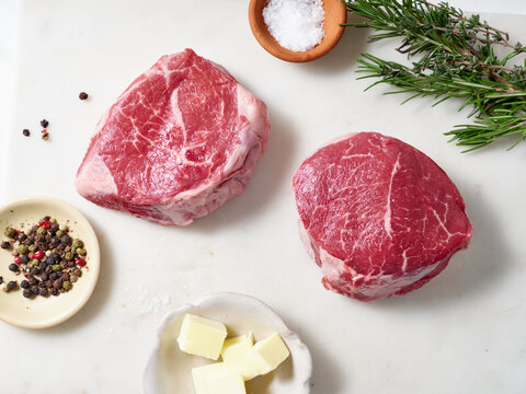 Raw chuck tender steak placed on a marble cutting board with salt, pepper, herbs, and butter ready for cooking in the kitchen