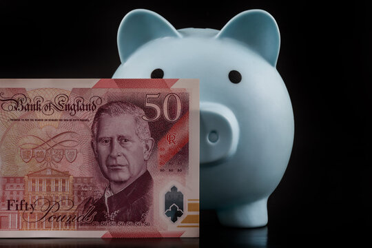 Blue piggy bank and 50 British pound note on a black background