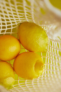 Fresh lemons in a net against a vibrant yellow background
