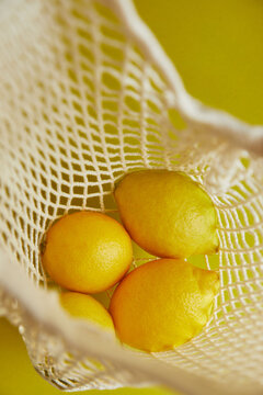 Fresh lemons in a mesh bag against a yellow backdrop