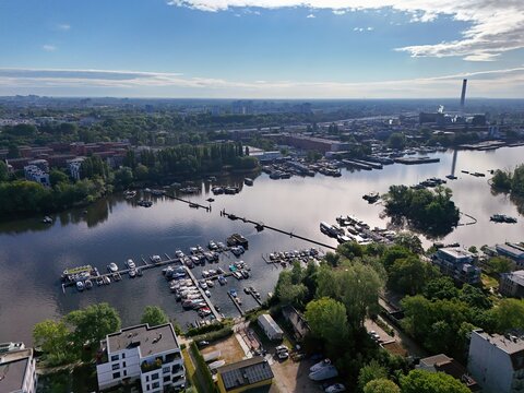 Aerial view of the shimmering Spree river winding through lush greenery, with boats docked near Alt-Stralau under a vast sky, Berlin, Berlin, Germany.