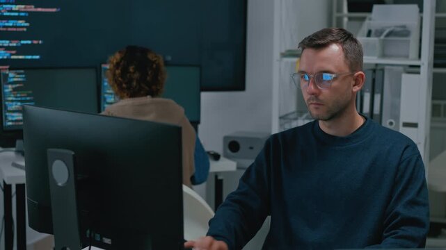 Focused diverse software engineers and AI developers working on code on computer screens in a dark office. Concept of machine learning, digital transformation, and future technology innovation.