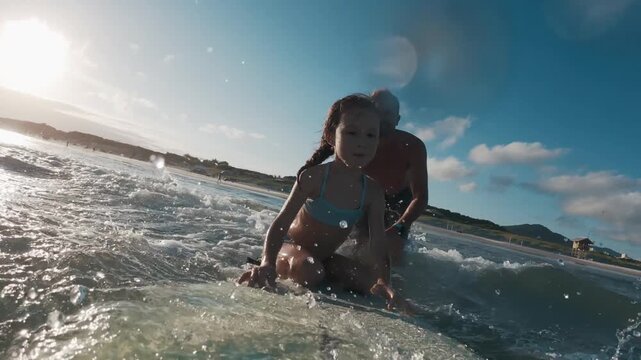 Kid surfs. Little girl learns surfing with her father and tries to keep balance on the surf board