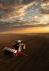 Farmer with tractor seeding crops at field on sunset