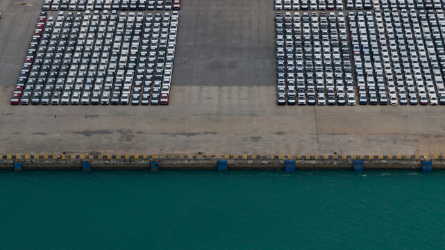 Aerial view of tightly packed rows of cars on the concrete pier edge meeting the turquoise waters, Tambon Thung Suk La, Chang Wat Chon Buri, Thailand.