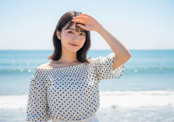 眩しい日差しの下で海を背景に微笑む水玉ブラウスの女性