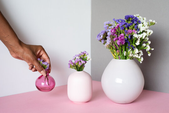 Colorful flowers in modern vases on pink surface