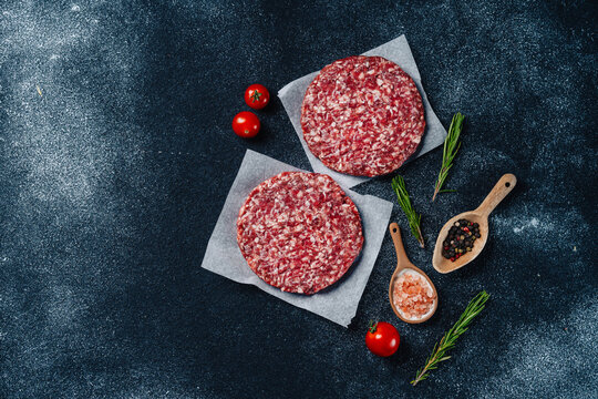 Raw veal burger patties on parchment with spices and herbs